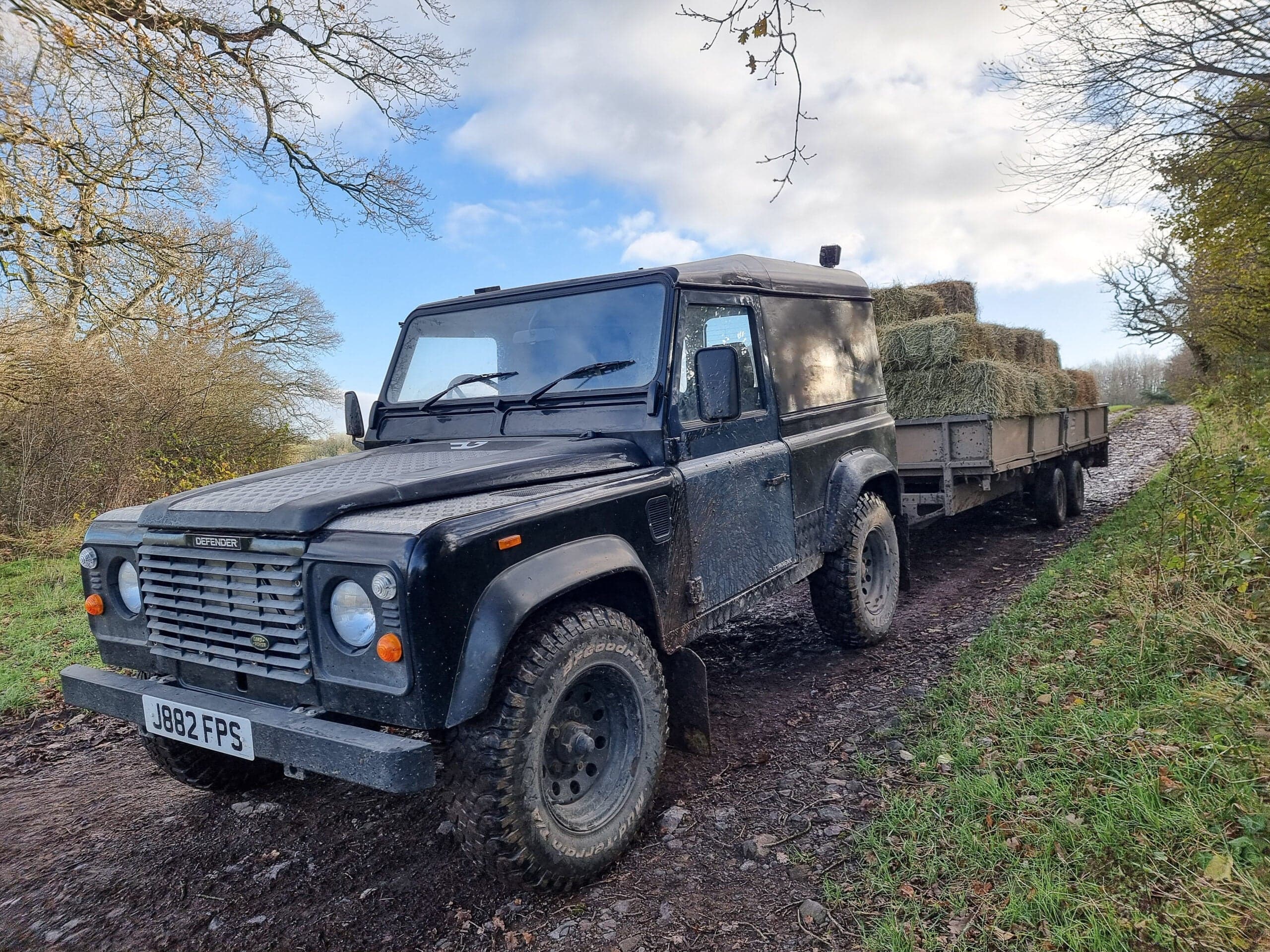 One of the converted Land Rover Defenders towing bales of hay loaded on a trailer