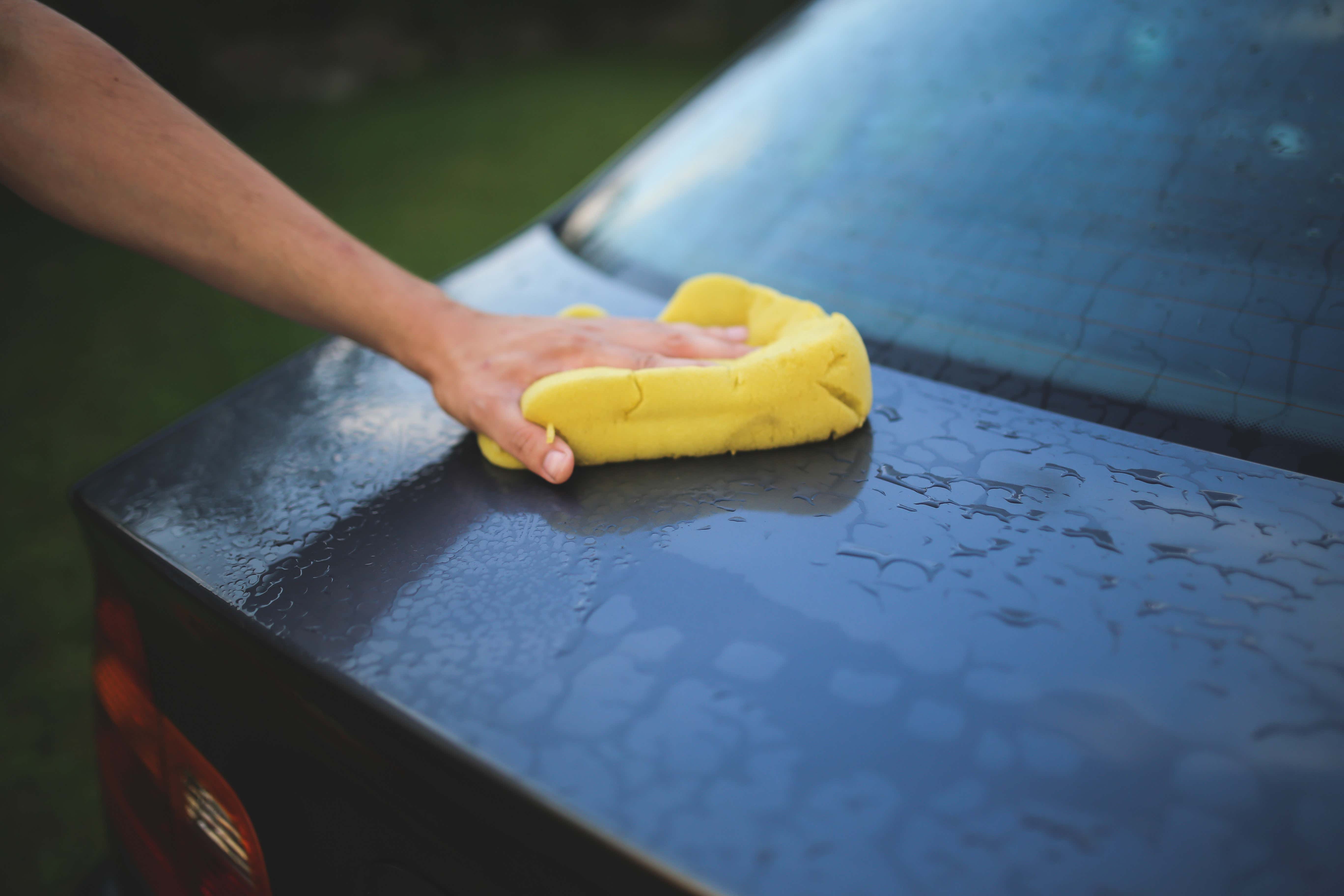 Washing a blue car with a yellow sponge