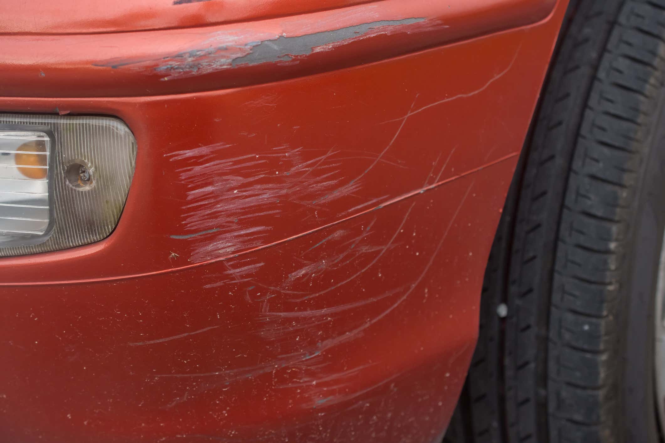 Red bumper car scratched with deep damage to the paint.