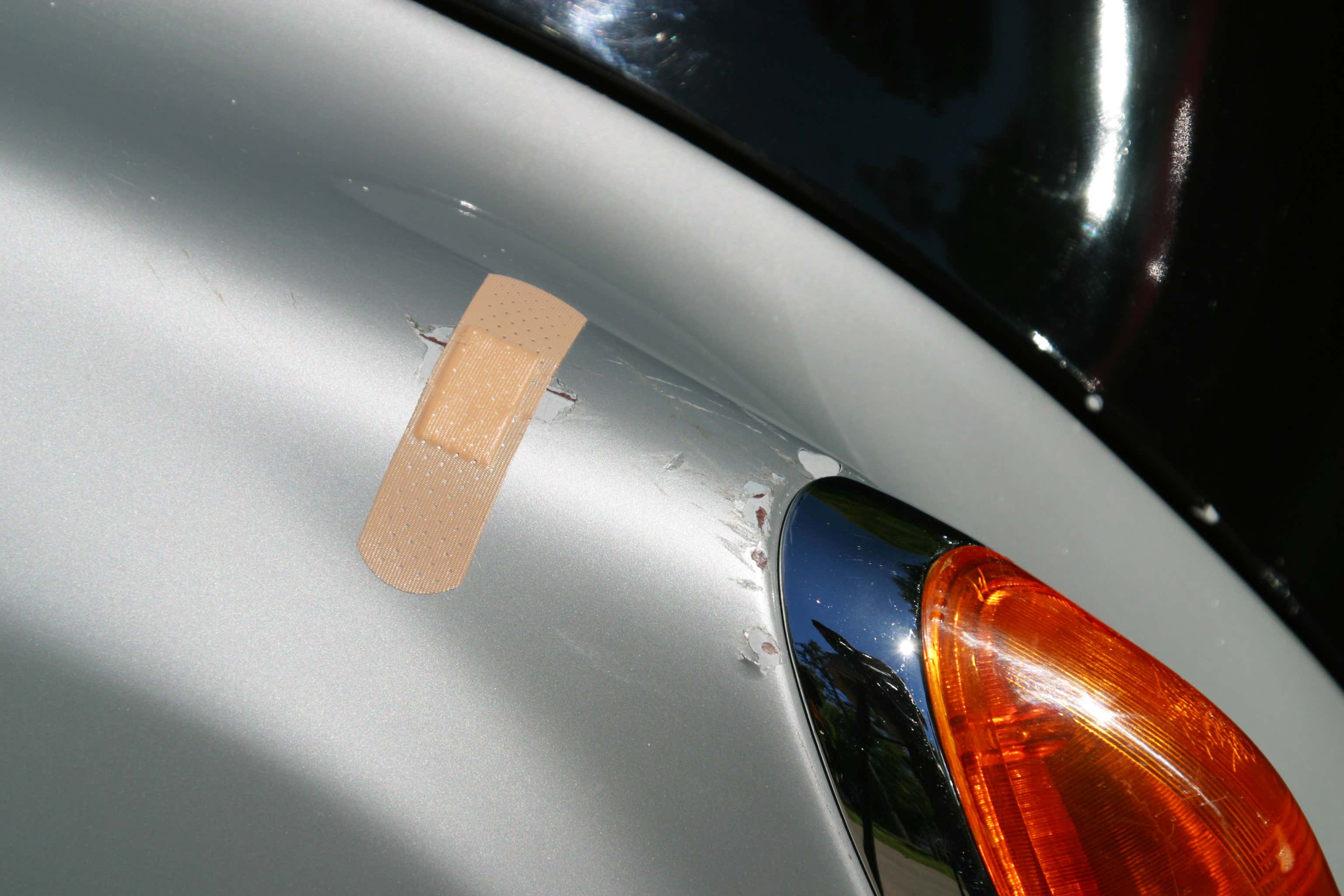Band-Aid being used to cover a scratch on side of a silver car