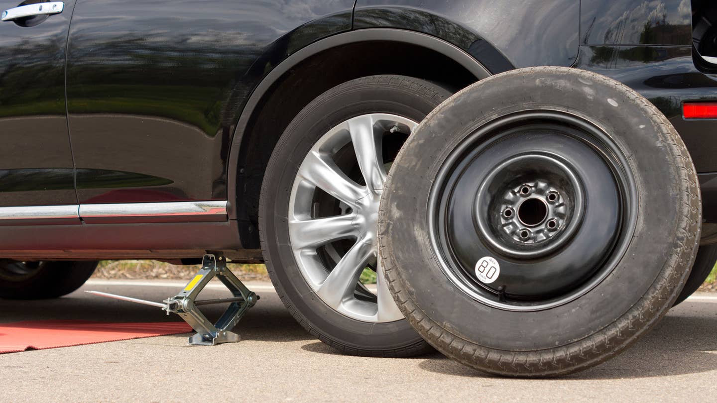 A flat tire placed next to a jacked-up car.