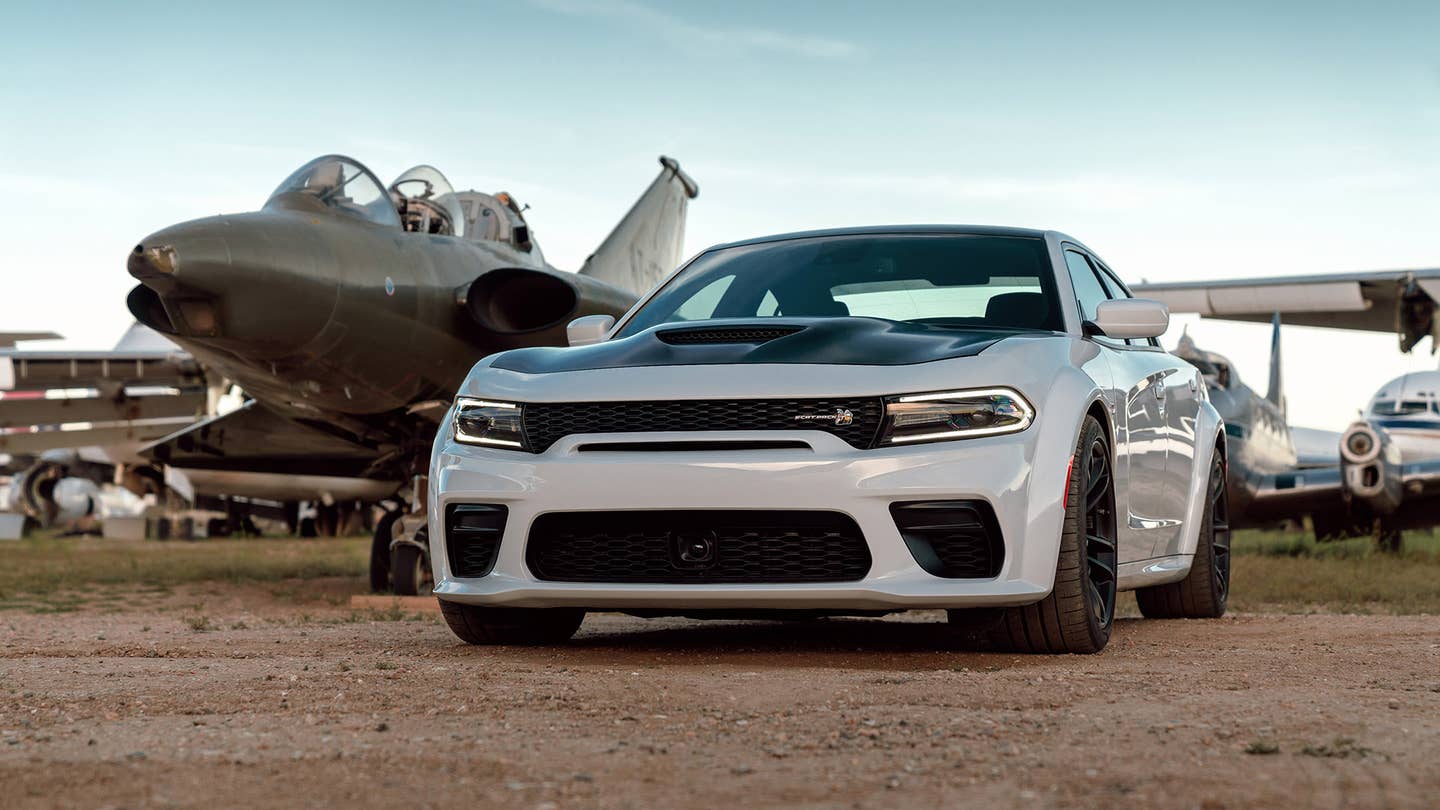 A white 2021 Dodge Charger Widebody Scat Pack rests next to a jet fighter.