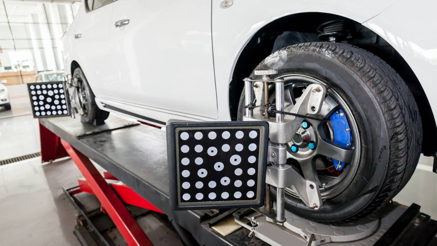 A car sits on a lift with wheel alignment tools attached.