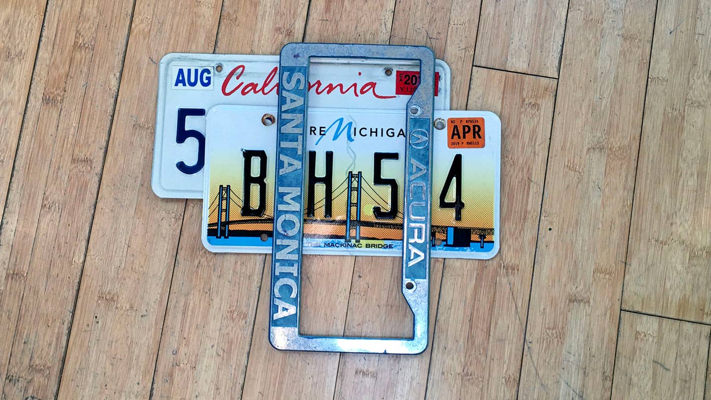 On a bamboo wood floor, a Michigan license plate sits on top of a California license plate.
