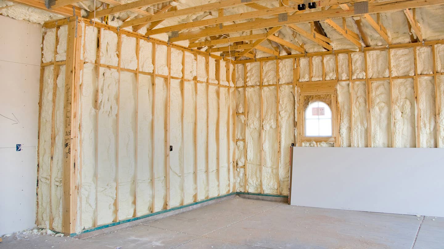 Insulation inside wooden framing contrasts against a concrete floor in a garage.