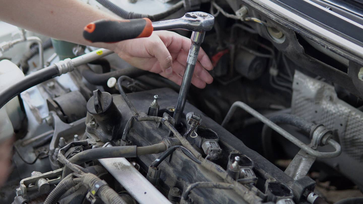 A mechanic removes spark plugs with a socket wrench.