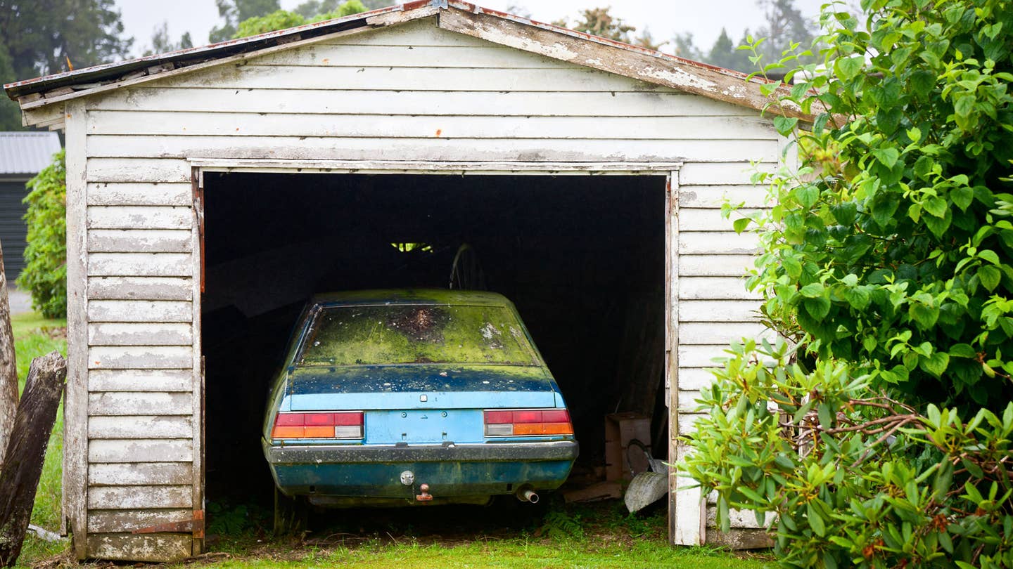 An abandoned European car is seen in a small garage with worn white paint.