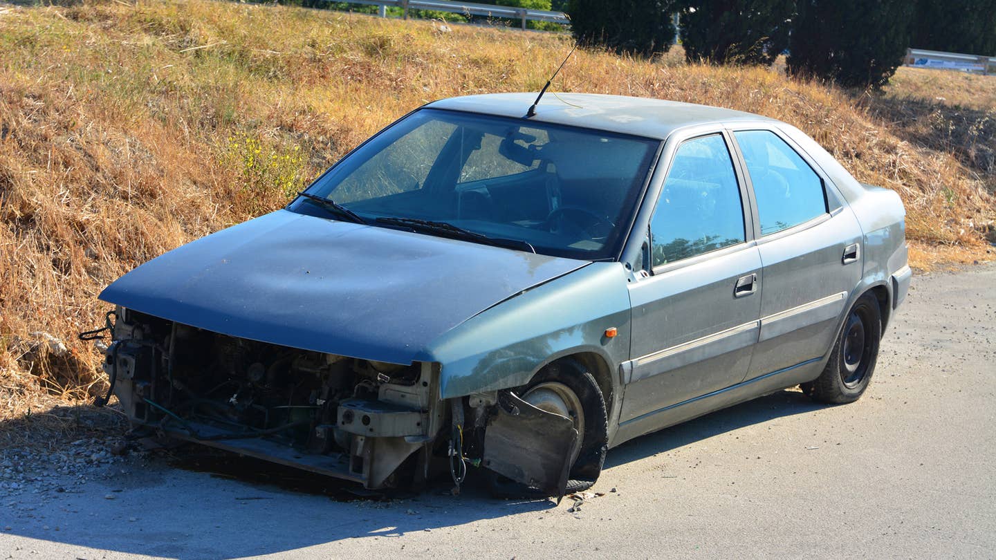 A busted car with no front end sits on the side of the road.
