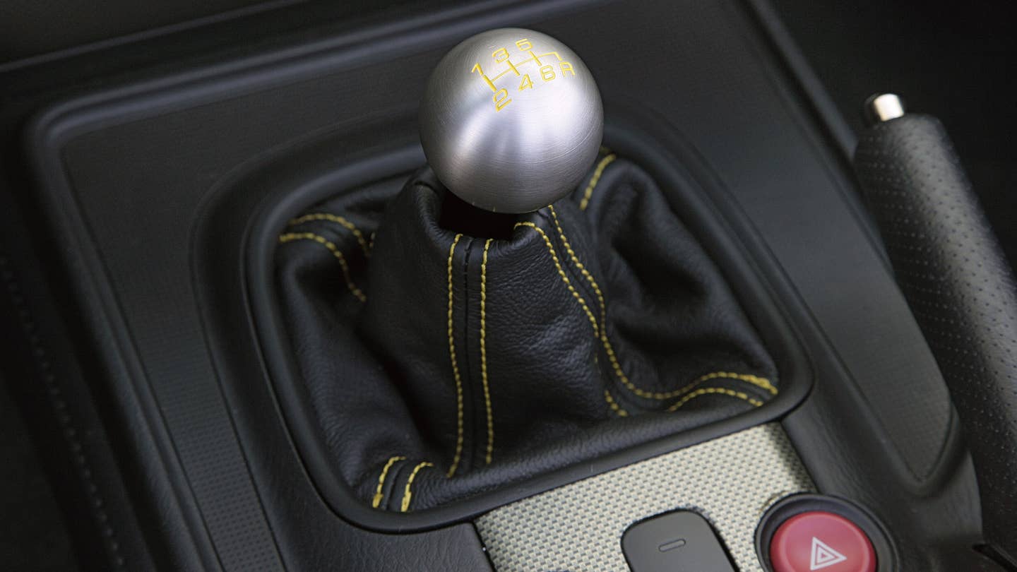 A metal ball shifter sits atop a black shift boot with yellow contrast stitching.