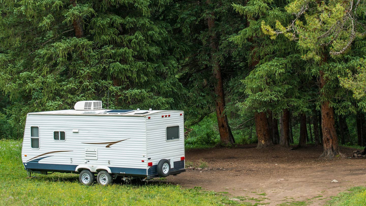 A white camper parks next to some woods.