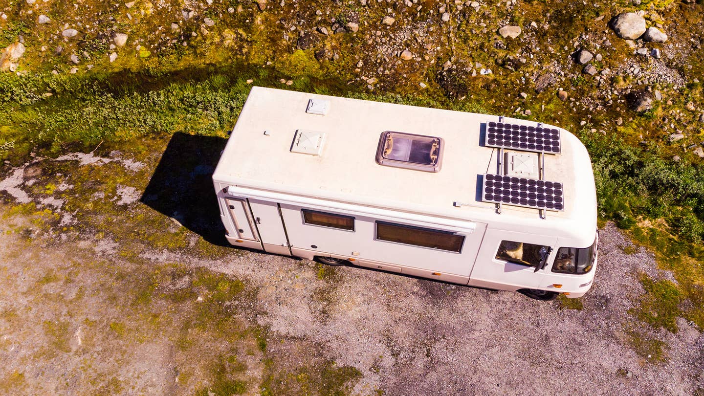 An RV with solar panels sits parked in nature.