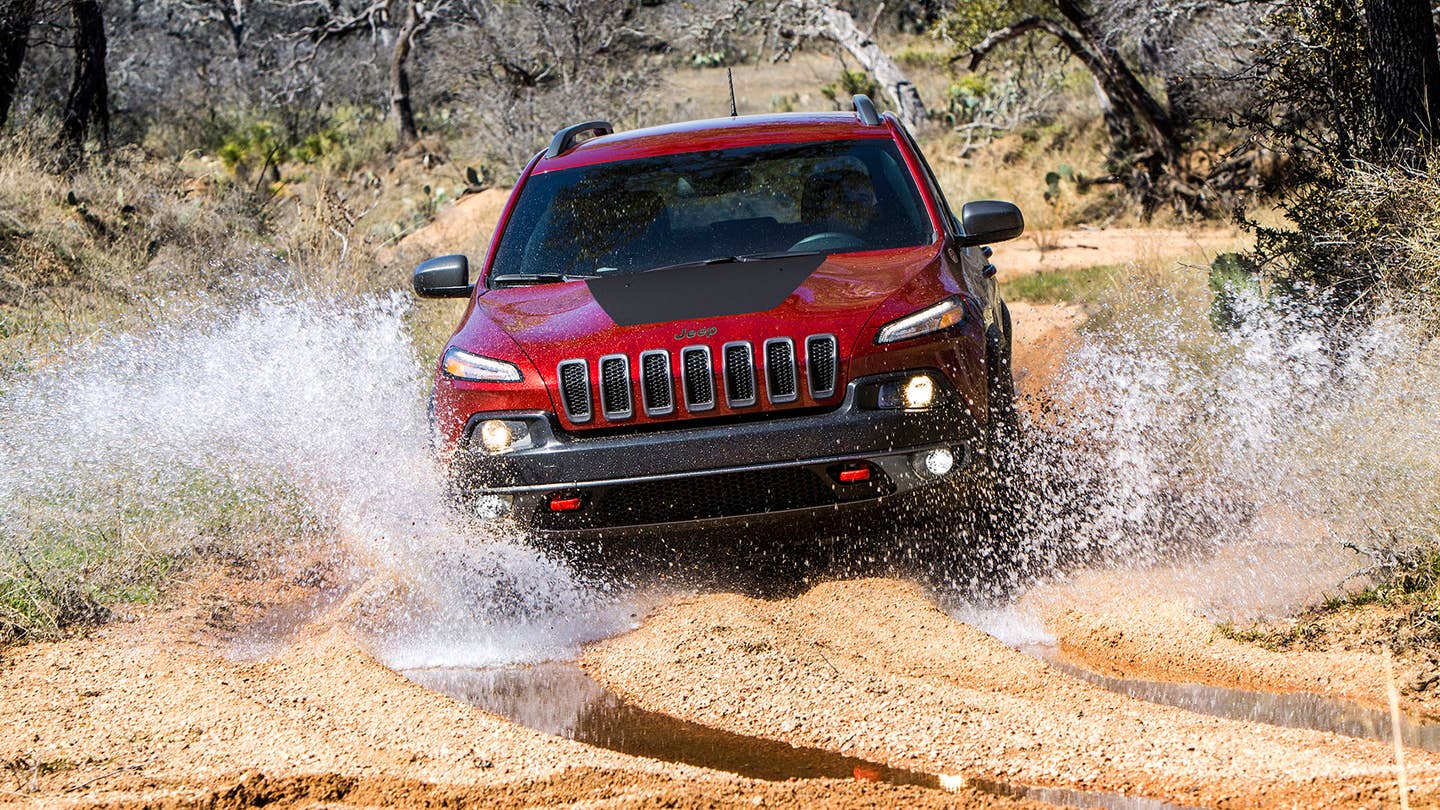 A red Jeep Cherokee splashes in the mud.