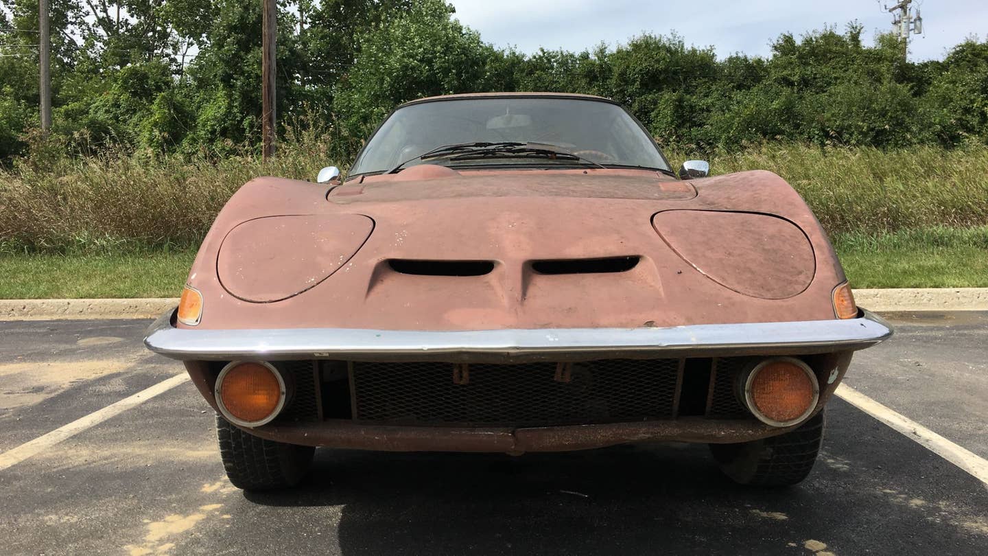 The front end of a rusty Opel GT sitting in a parking lot.