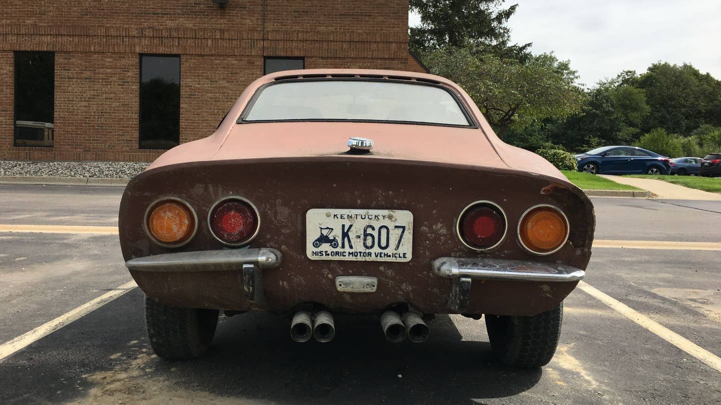 The rear end of a rusty Opel GT sitting in a parking lot.
