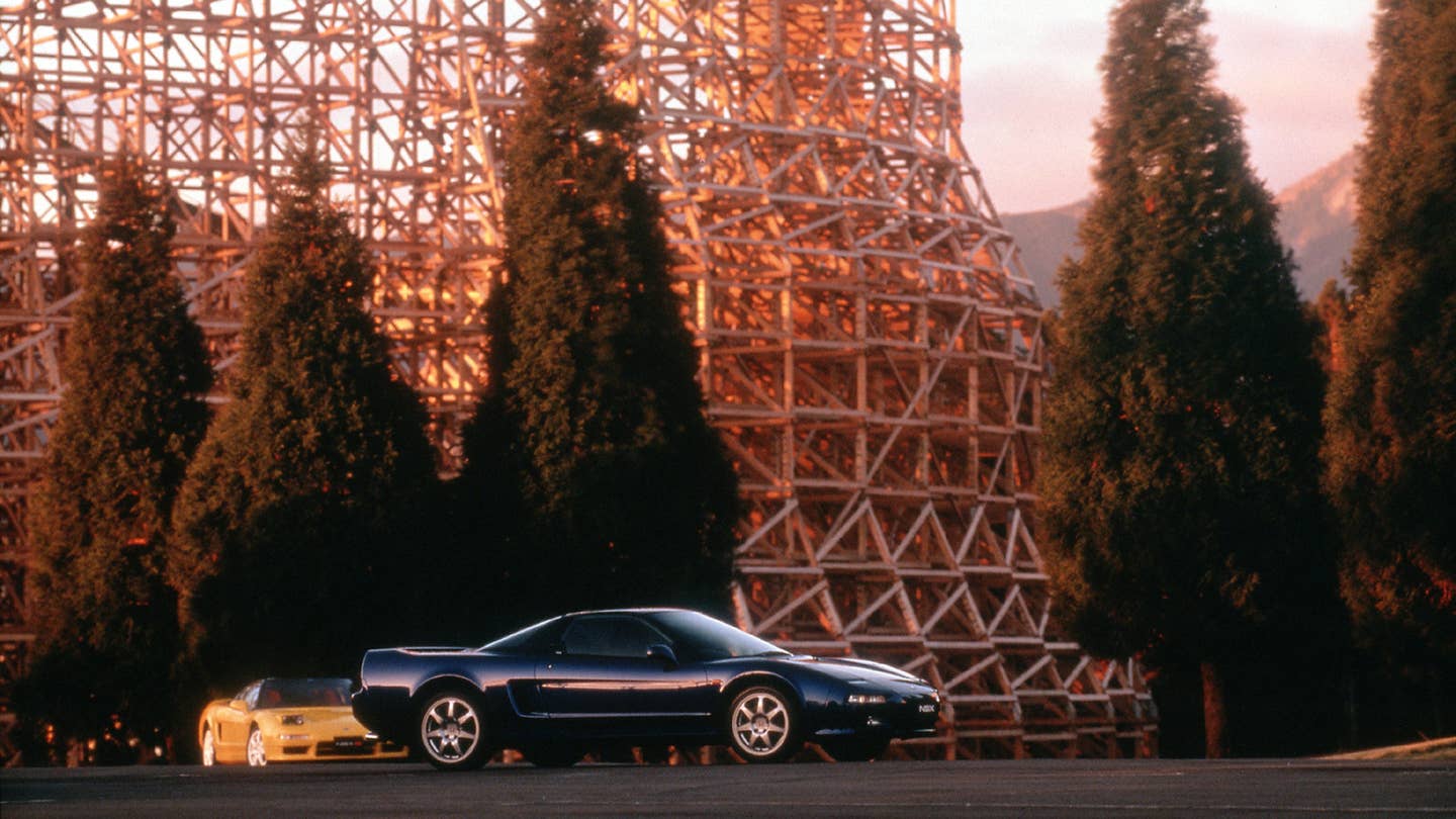 Two Acura NSXes playing tag in front of a wooden roller coaster.