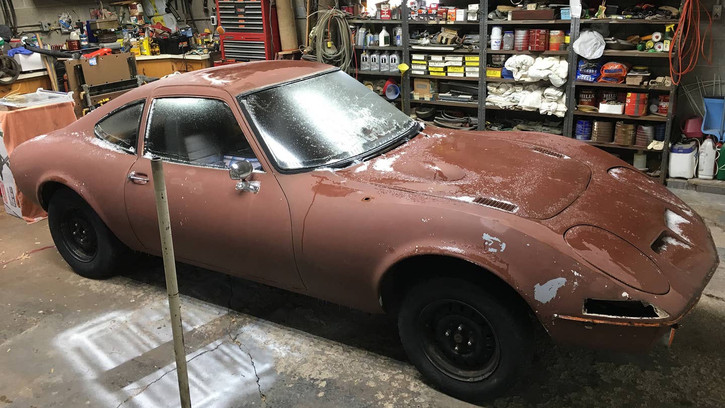 A brown Opel GT in a chaotic garage.