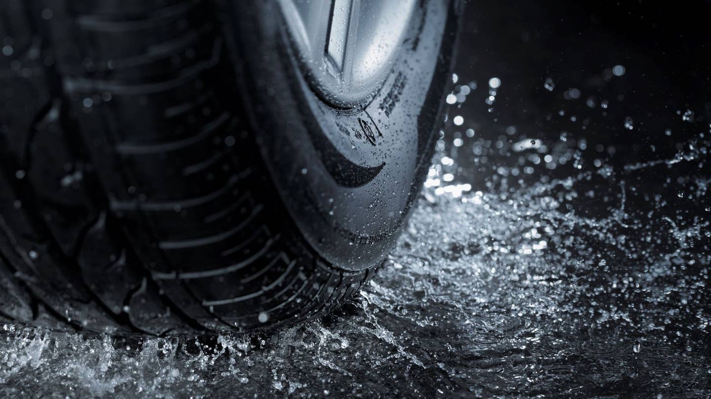 A detailed view of a tire's tread and sidewall as it splashes through water.