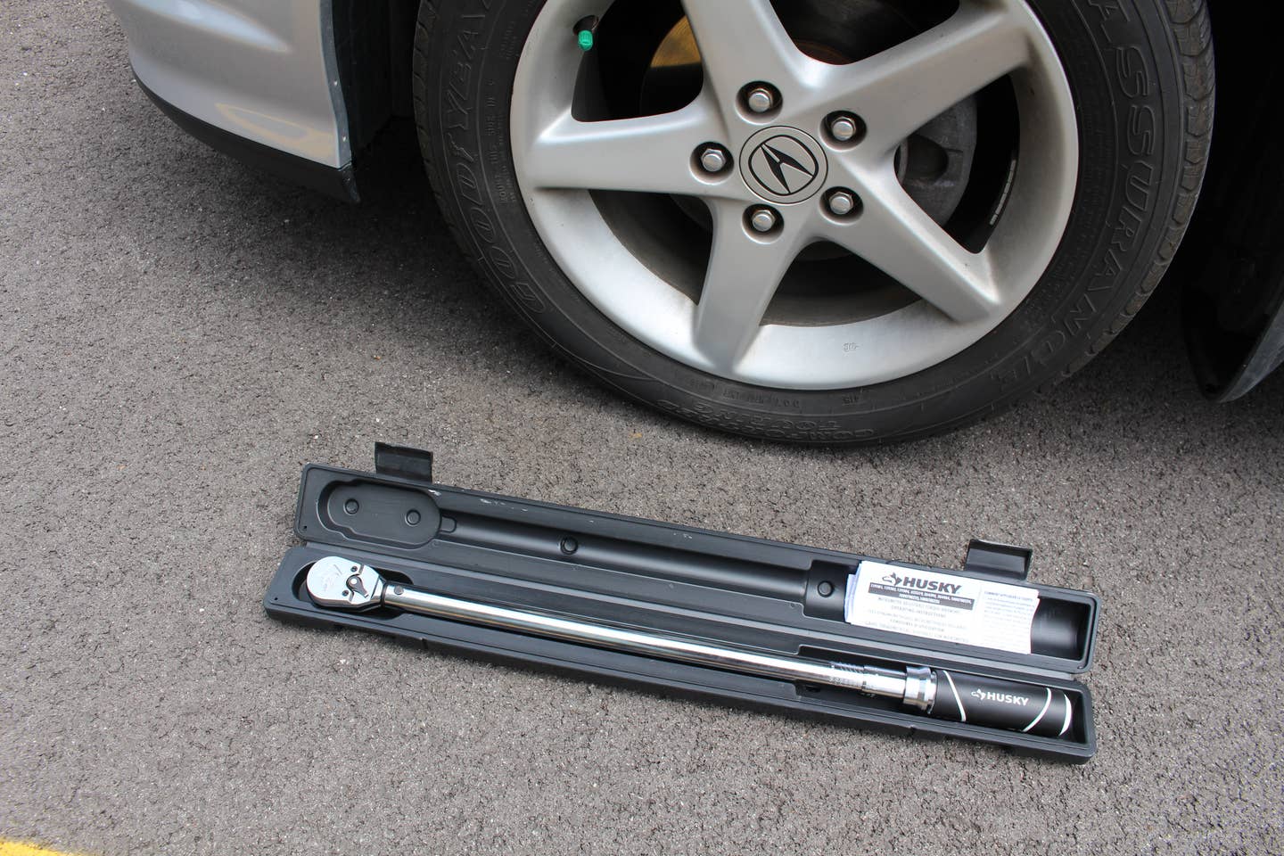 A husky torque wrench in its case on the ground next to an Acura RSX wheel.