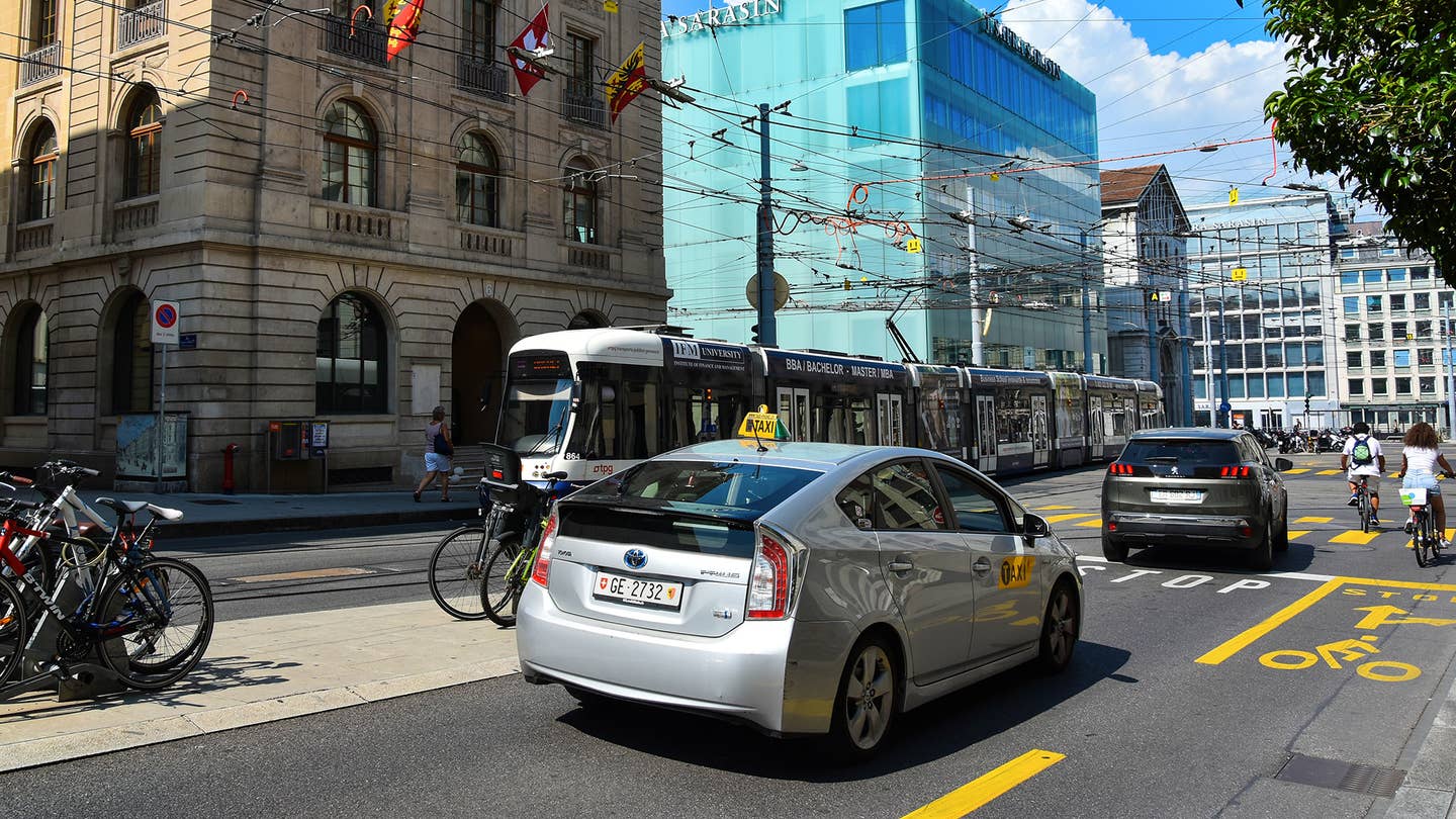 A silver Toyota Prius stops behind a Peugeot at a busy city intersection.