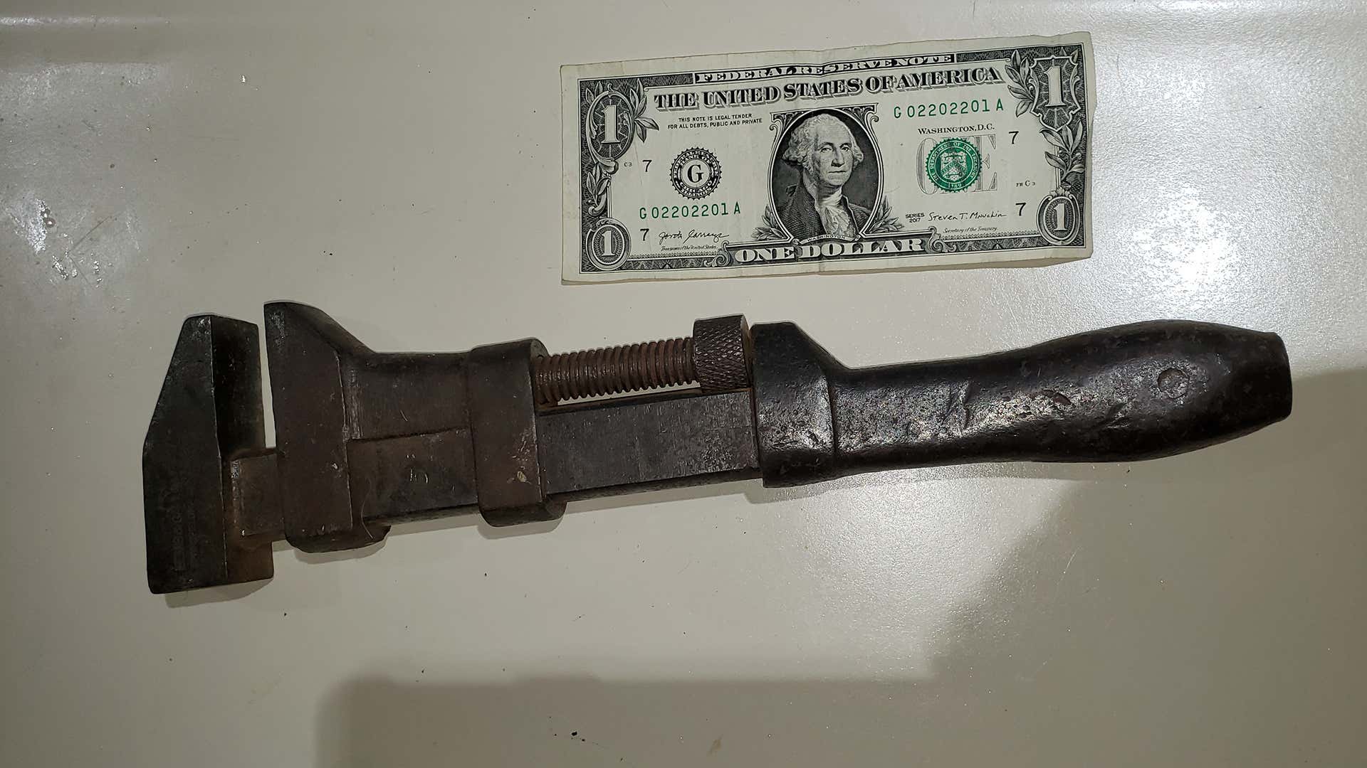 An old railroad wrench next to a dollar bill.