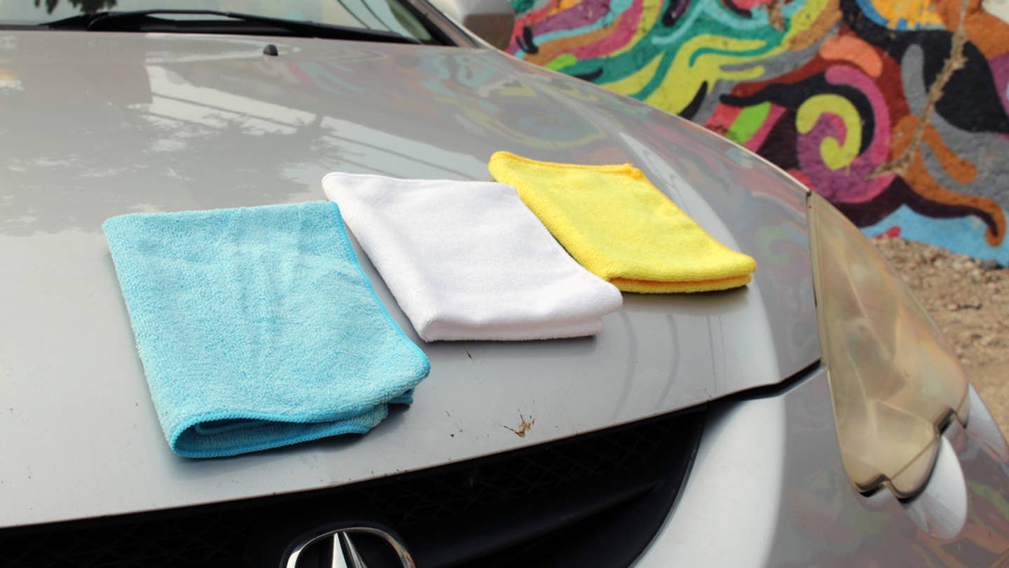 Blue, yellow, and white microfiber towels on the hood of a silver 2003 Acura RSX.