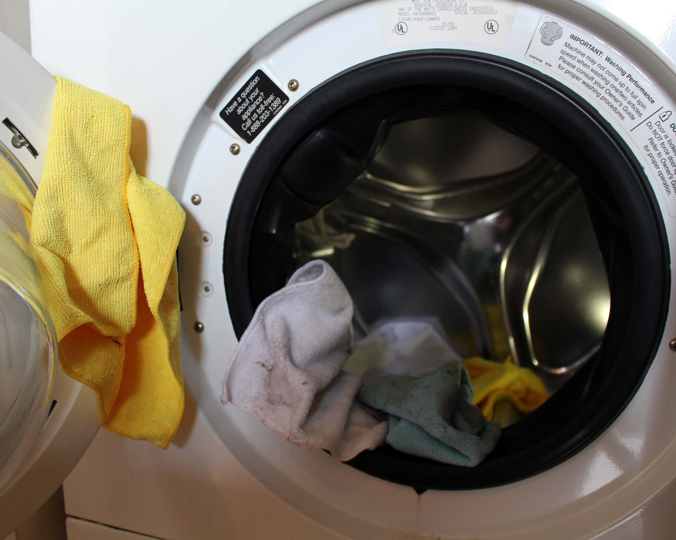Blue, yellow, and white microfiber towels hanging out of a white front-load washing machine.