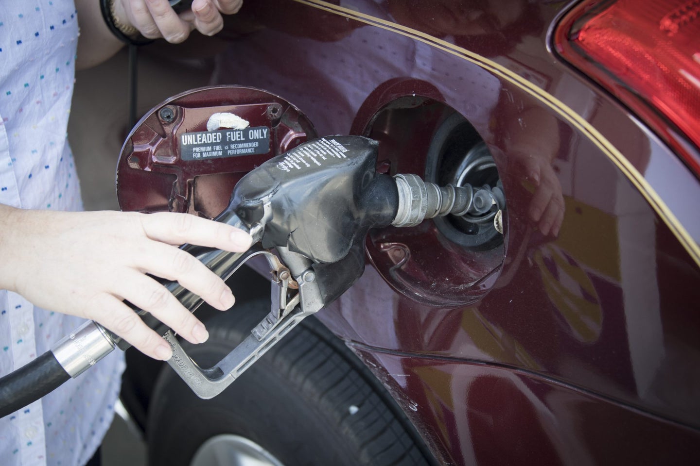 Woman's hand holding a pump nozzle in car fuel tank door.