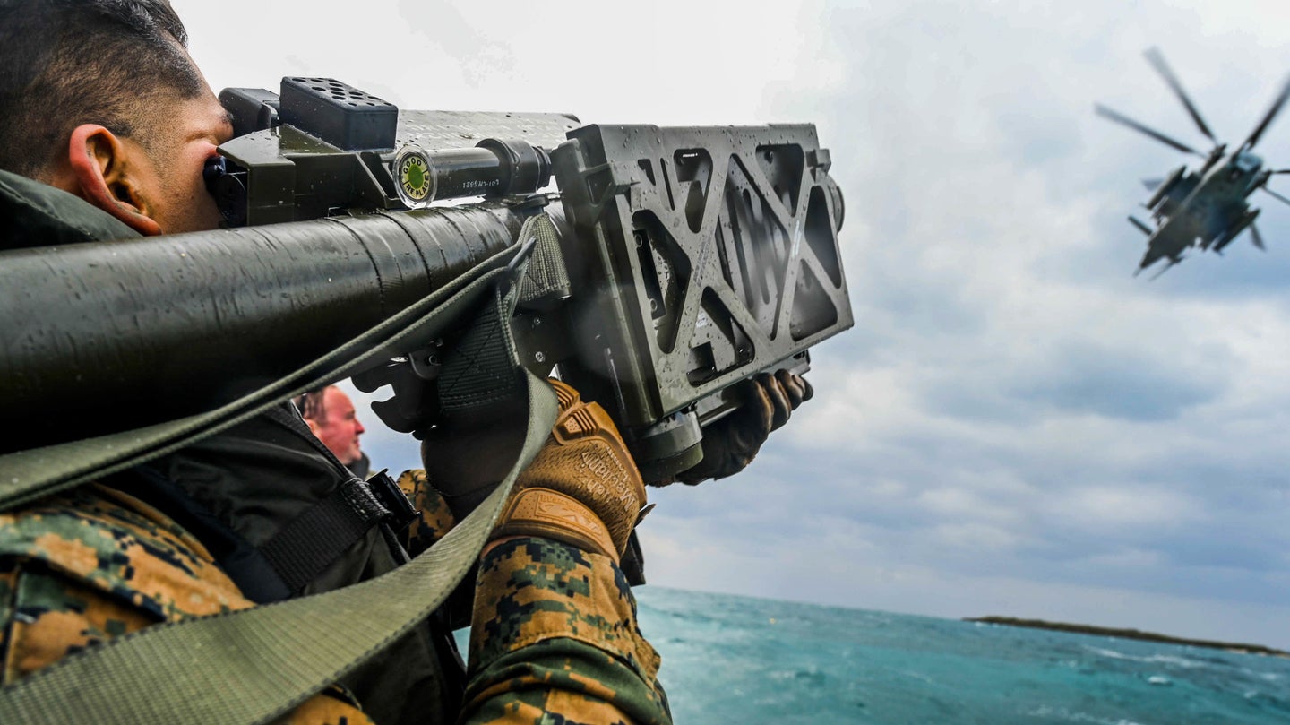 A Marine riding in a rubber raft aims a Stinger missile launcher at CH-53E helicopter during an exercise.