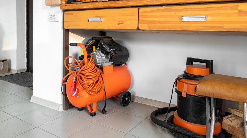 Small portable air compressor at home warehouse garage under wooden workbench