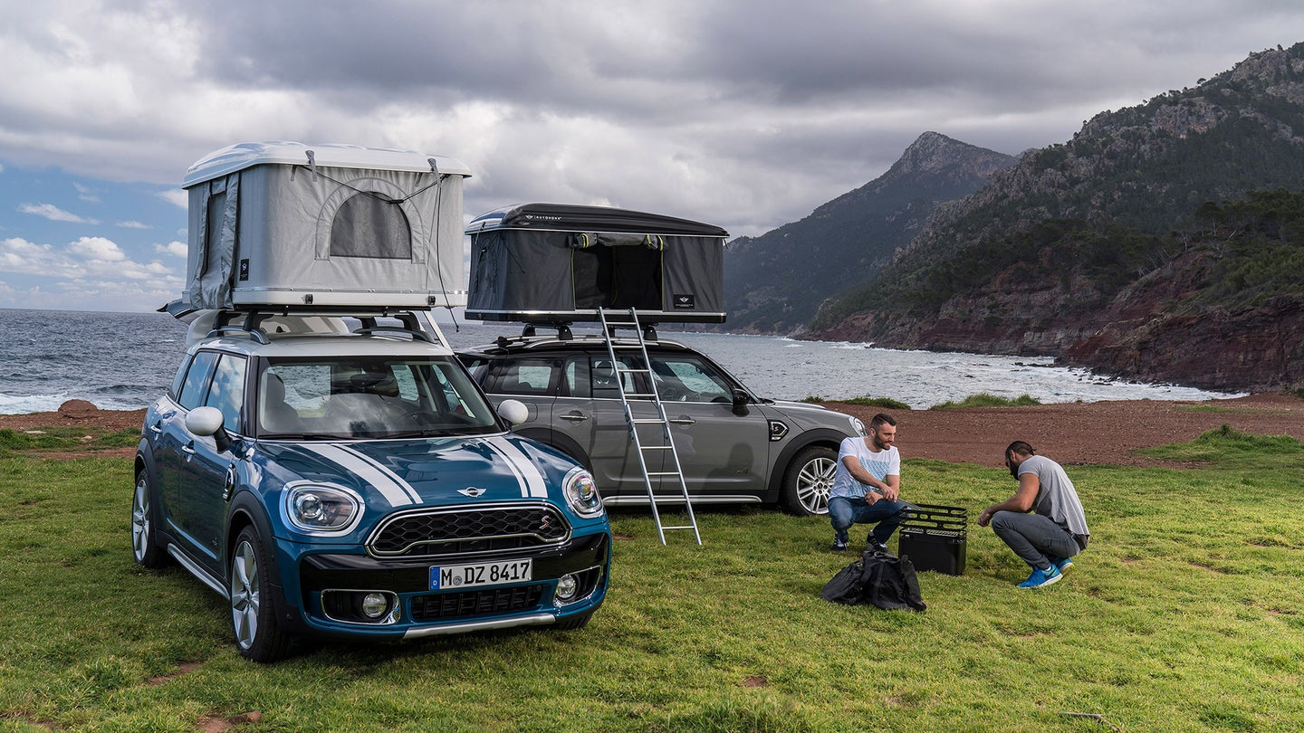 Two Mini Cooper Countrymans with rooftop tents next to the ocean and a campfire with two guys.