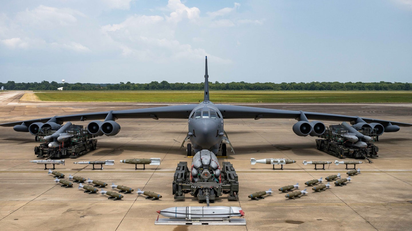 A B-52H bomber posed in front of an array of ordnance that it can carry.