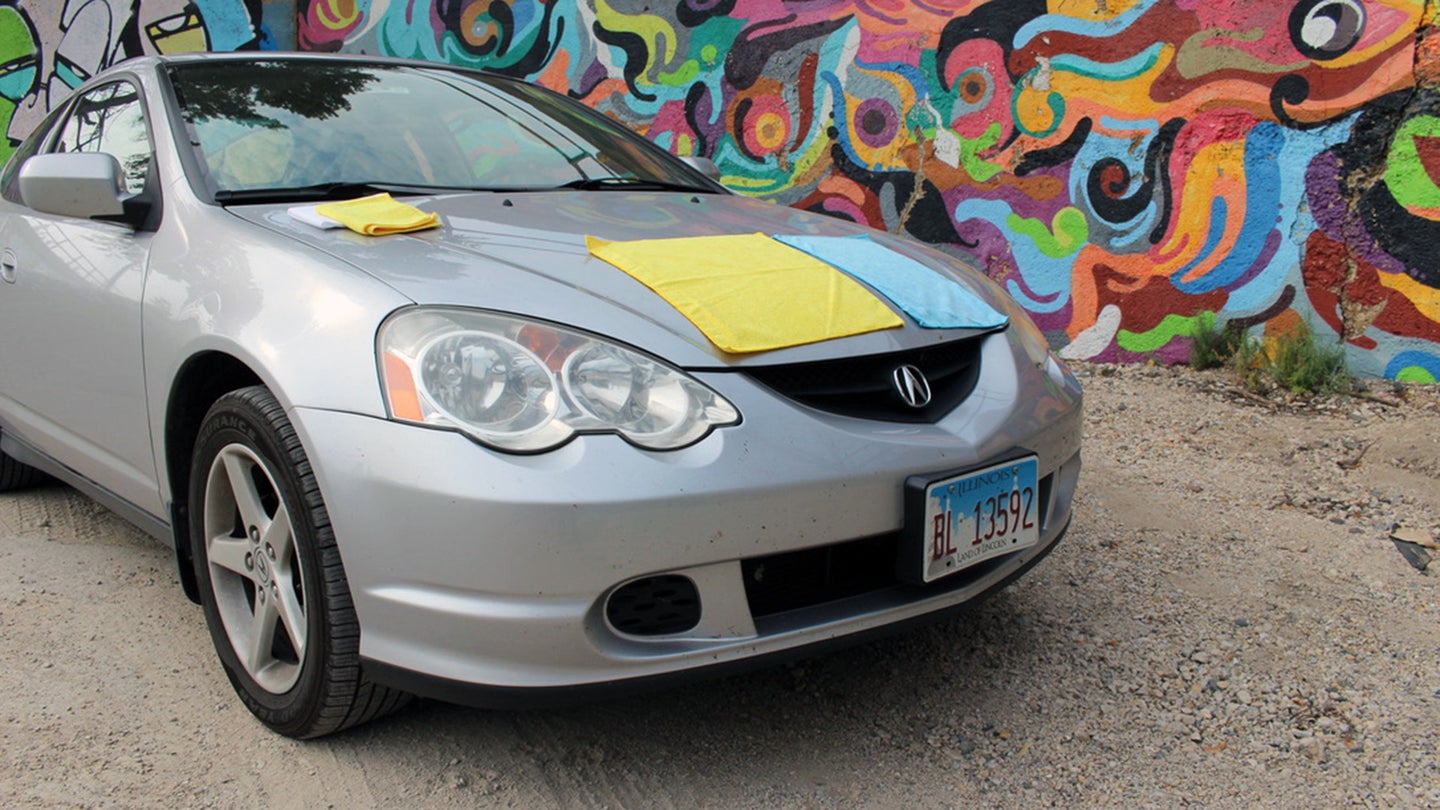 Blue, yellow, and white microfiber towels on the hood of a silver 2003 Acura RSX.
