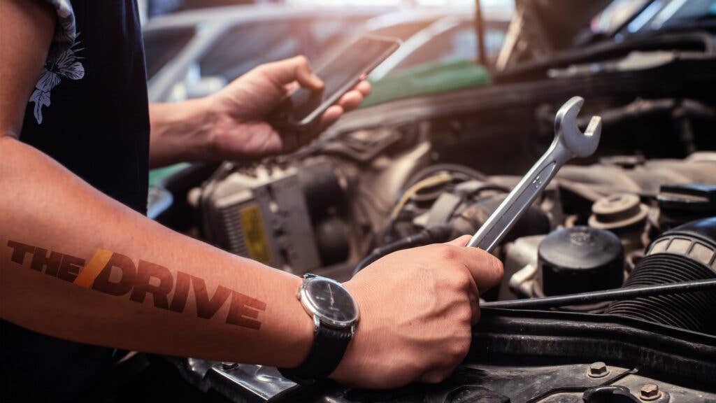A mechanic references a phone while looking at a car engine.