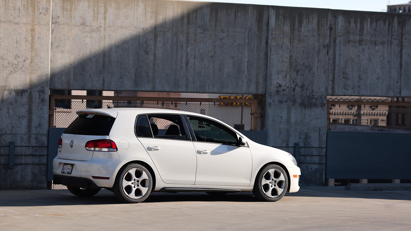 A 2010 Volkswagen GTI sits beneath a sunbeam. Concrete support beams washed with rust in the background.