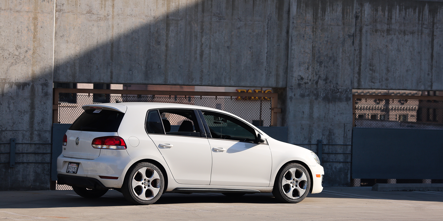 A 2010 Volkswagen GTI sits beneath a sunbeam. Concrete support beams washed with rust in the background.