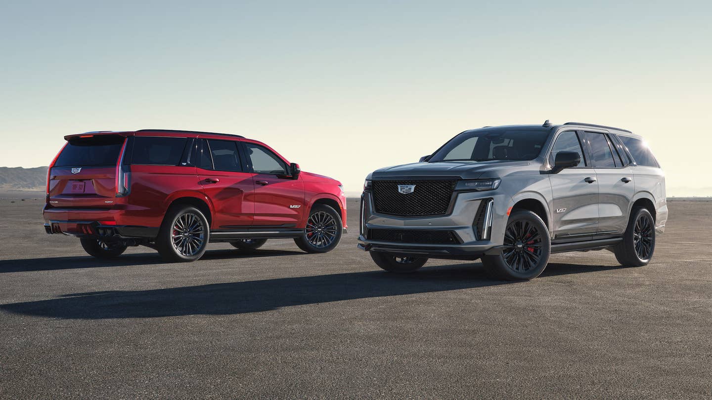 2023 Cadillac Escalade-Vs, one grey one red, facing opposite directions around sunset