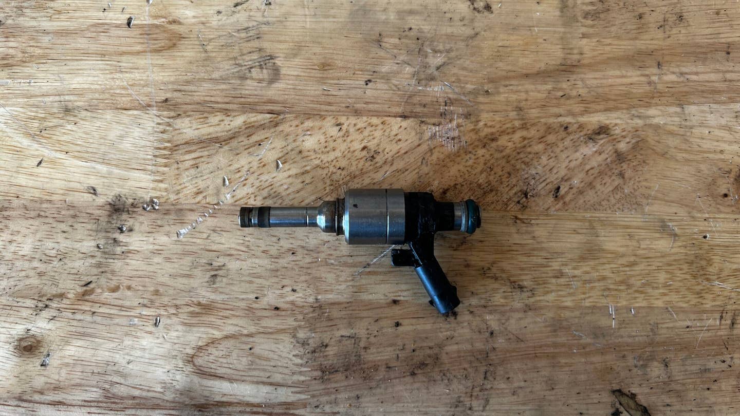 A fuel injector for a Volkswagen TSI engine. It is sitting on a birch workbench.