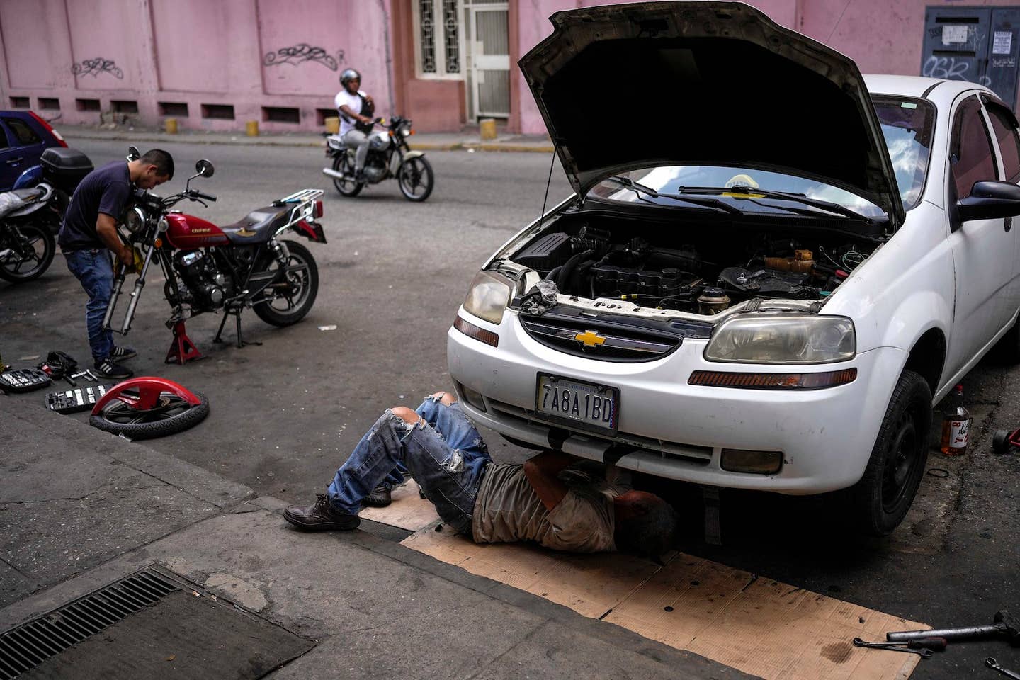 Carlos Valero repairs his car's exhaust system, in the San Agustin neighborhood of Caracas, Venezuela, Tuesday, April 19, 2022. Drivers try to coax a little more life out of aging vehicles in a country whose new car market collapsed and where few can afford to trade up for a better used one. (AP Photo/Matias Delacroix)