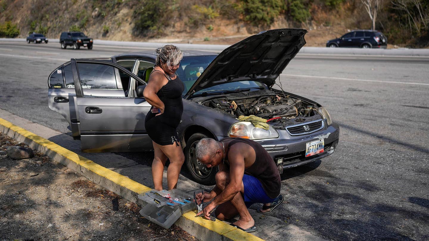 A man tries to repair his car, parked on the side of the road that connects La Guaira with Caracas, Venezuela, Tuesday, April 19, 2022. Drivers try to coax a little more life out of aging vehicles in a country whose new car market collapsed and where few can afford to trade up for a better used one. (AP Photo/Matias Delacroix)