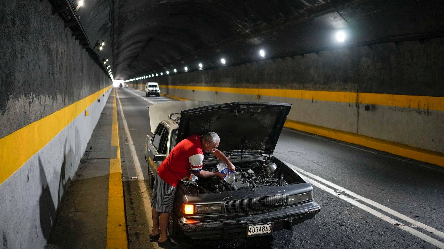 A man tries to cool down his overheating car by pouring water into the radiator, in one of the tunnels of the road that connects La Guaira with Caracas, Venezuela, Tuesday, April 19, 2022. Drivers try to coax a little more life out of aging vehicles in a country whose new car market collapsed and where few can afford to trade up for a better used one. (AP Photo/Matias Delacroix)