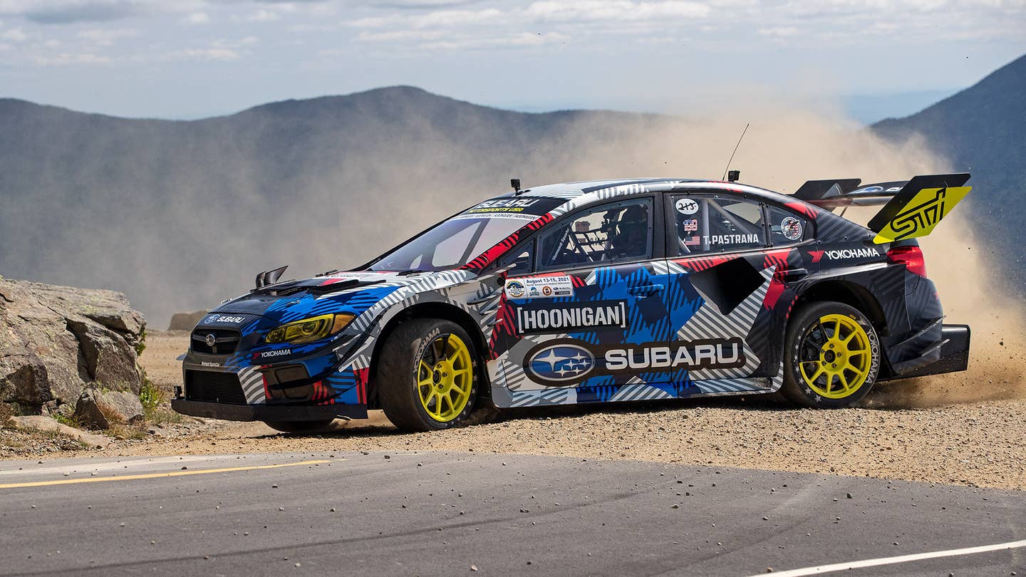 A Subaru WRX kicks up a cloud of dust as it drifts on dirt toward a patch of tarmac