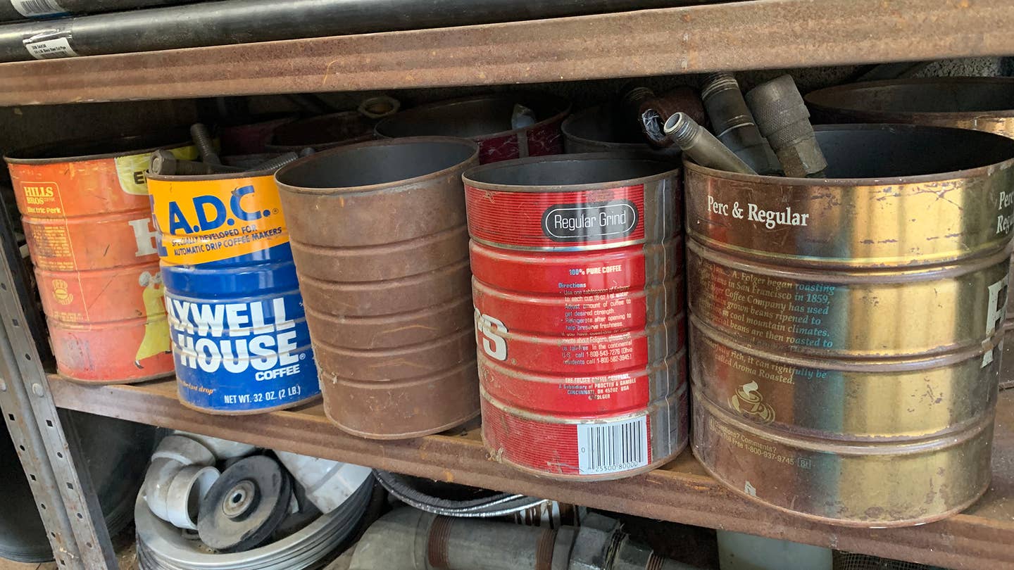 Five rusty old coffee cans on a shelf in a garage.