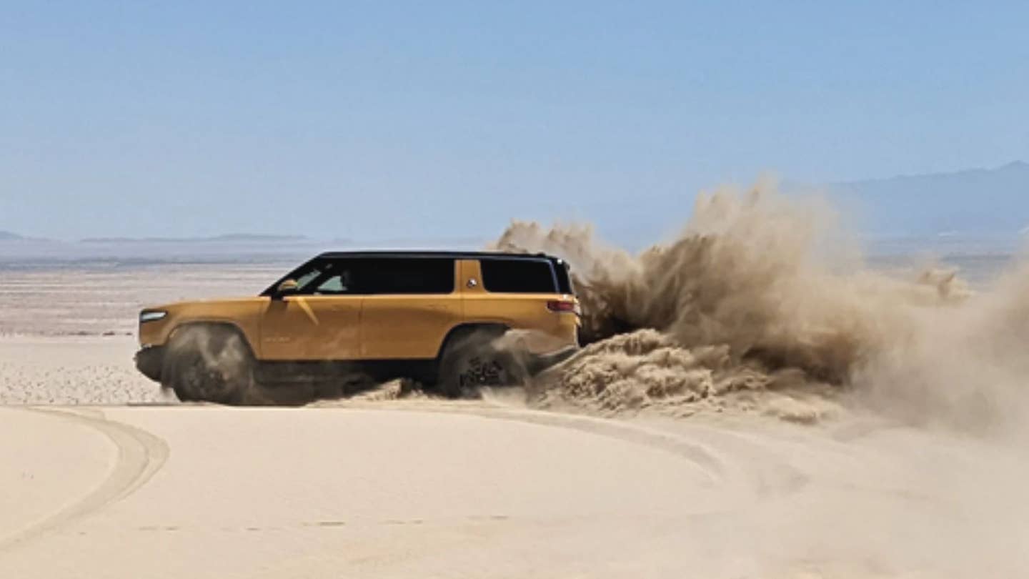 Yellow Rivian electric truck driving across sand
