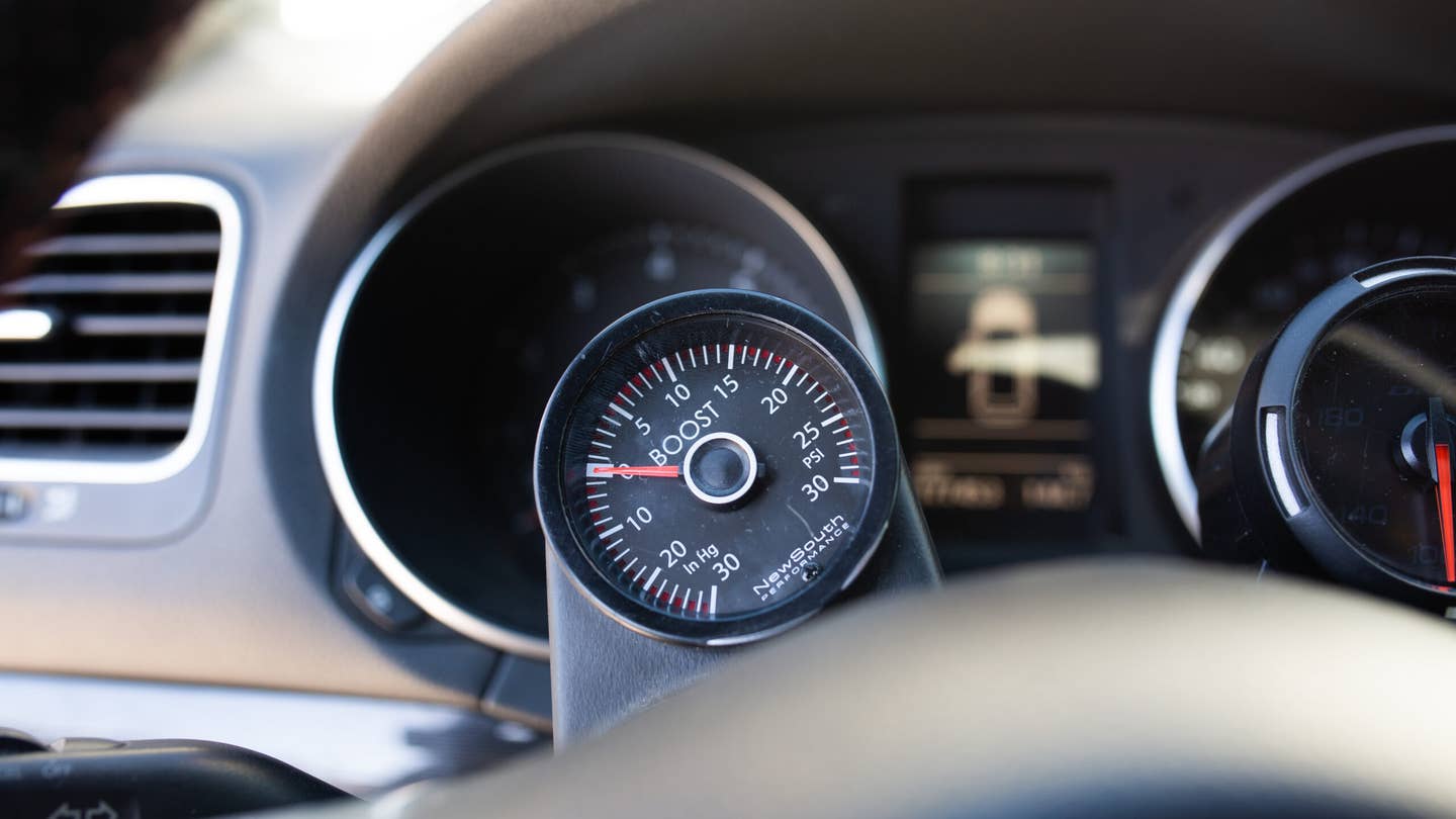 A boost pressure gauge mounted on the steering column of a Volkswagen GTI. The gauge reads up to 25 psi.