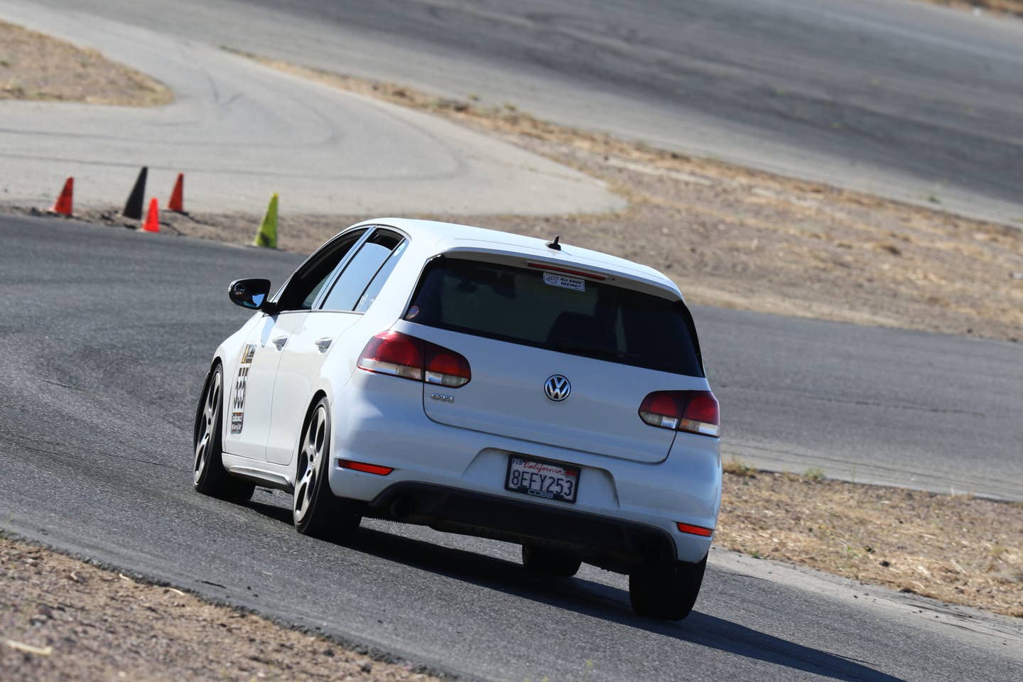 A rear view of a 2010 Volkswagen GTI driving on a desert race track.