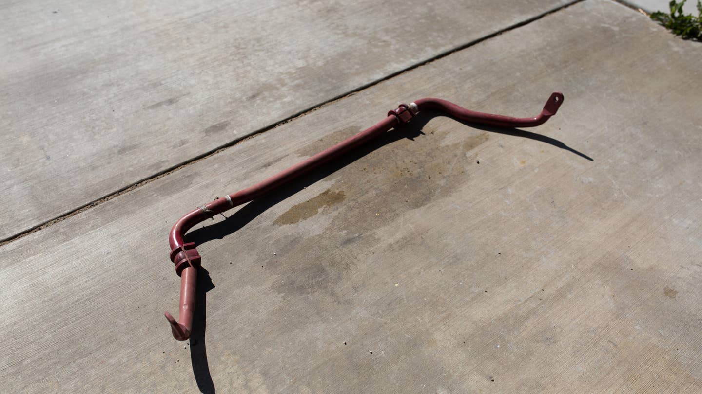 An anti-roll bar laying on oil-stained concrete.