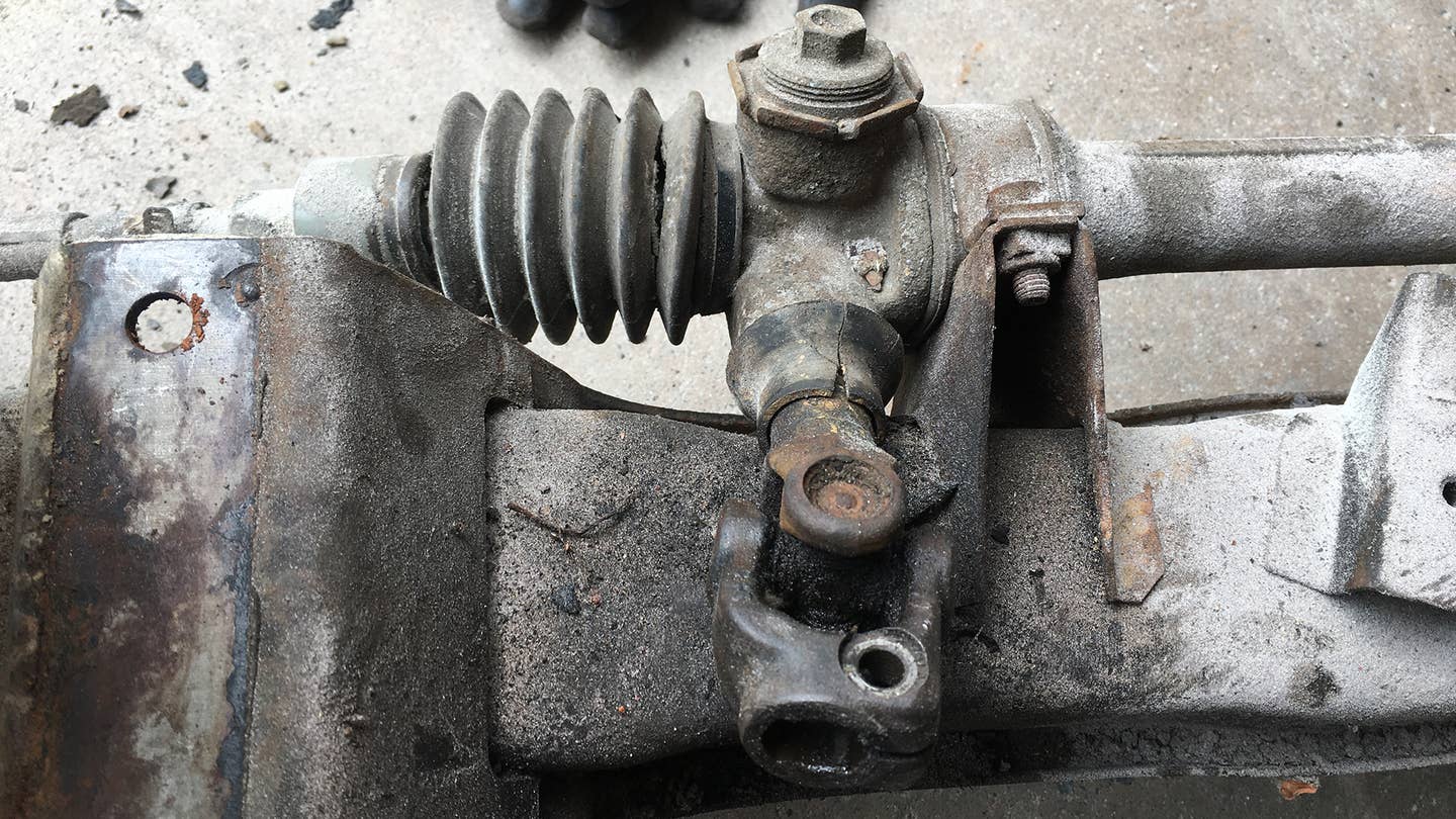 A rusty steering rack with dry-rotted rubber boots.