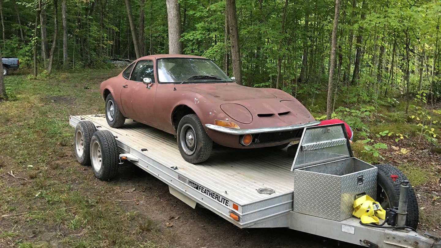 An Opel GT on a trailer in the woods.