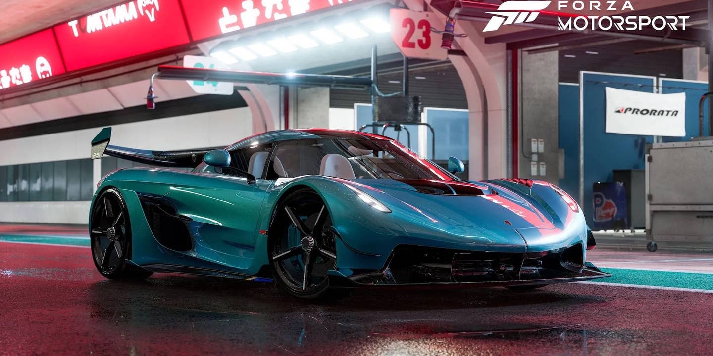 A teal, rain-soaked Koenigsegg Jesko poses dramatically under the lights of a race track pit lane.
