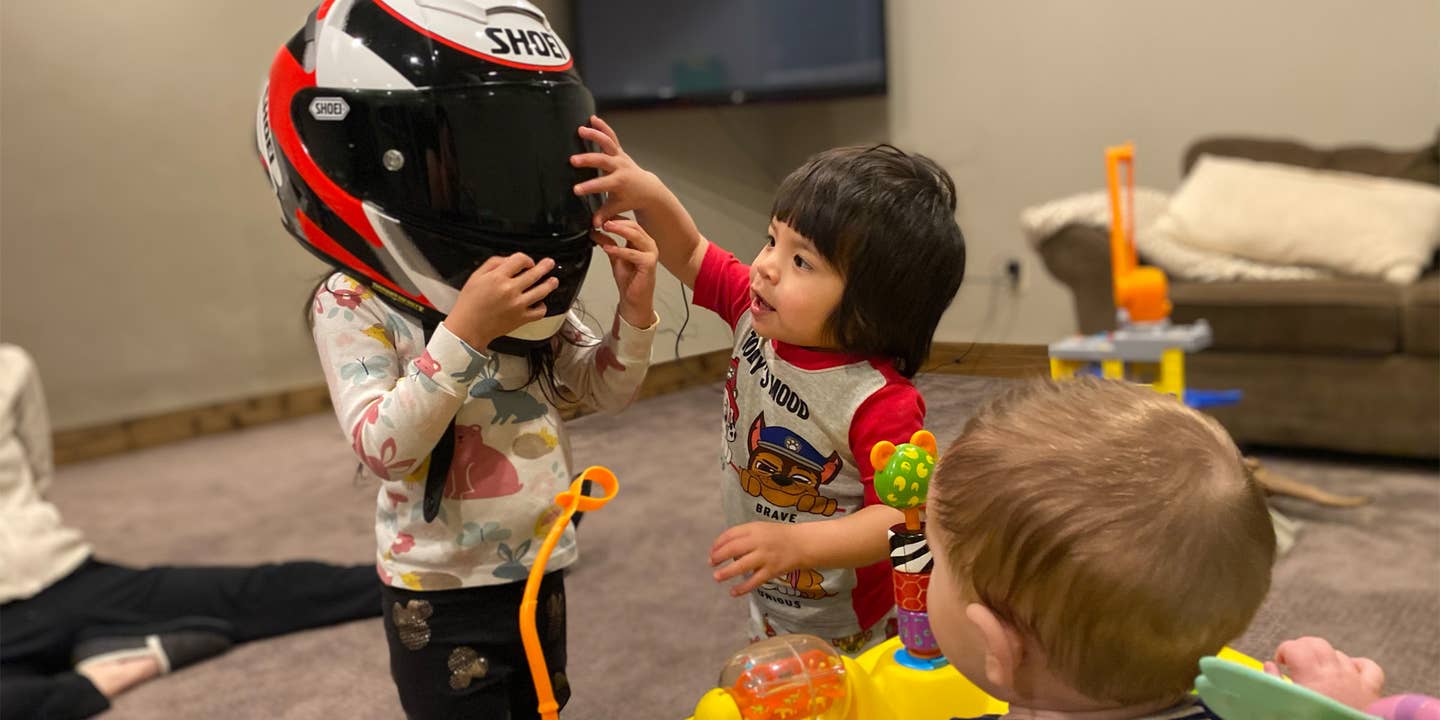 One child plays with a motorcycle helmet while two other children look on.